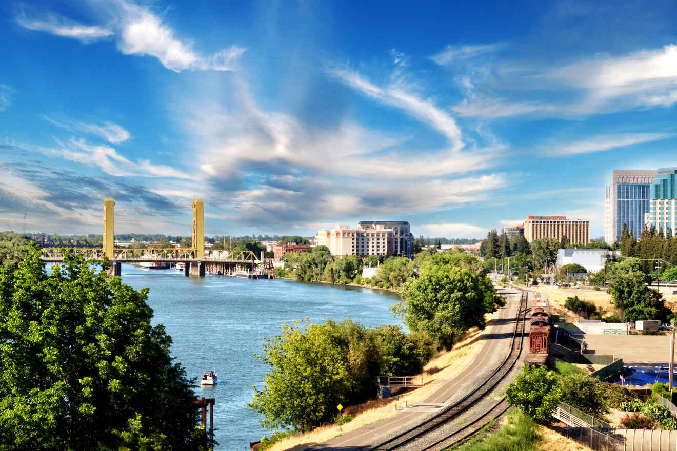 A scenic view of the Sacramento River with the Tower Bridge in the foreground, surrounded by lush trees and a clear blue sky, showcasing Sacramento's natural and urban blend.